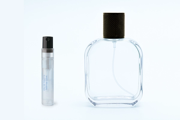 Kleines Parfum-Probefläschchen (Eau de Toilette) neben einem leeren Flakon auf weißem Hintergrund.
