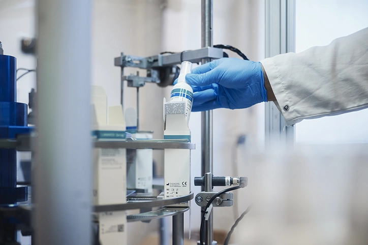 Employee in blue gloves takes a CE-marked medical device spray from the filling line.