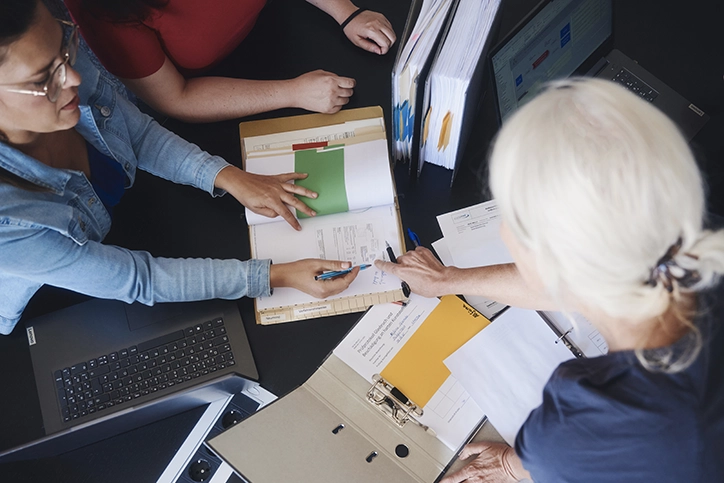 Drei Personen prüfen bei einem Audit Unterlagen und Aktenordner am Schreibtisch. Qualität und Zertifizierung bei ZSB.
