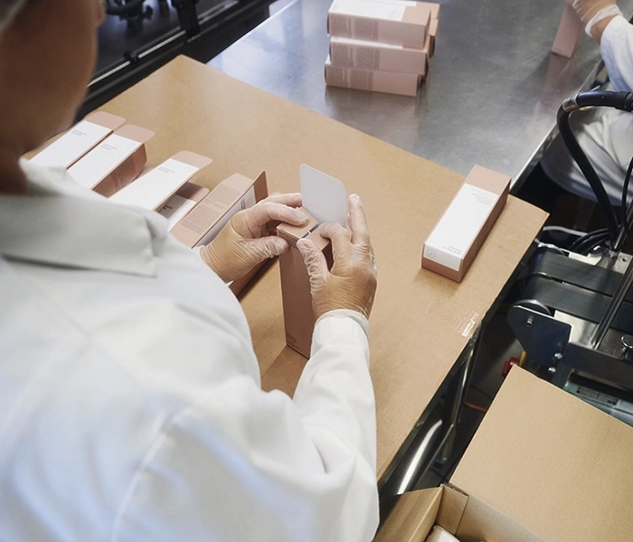 ZSB-Mitarbeiterin faltet und bestückt bei der Konfektionierung Faltschachteln am Verpackungstisch.