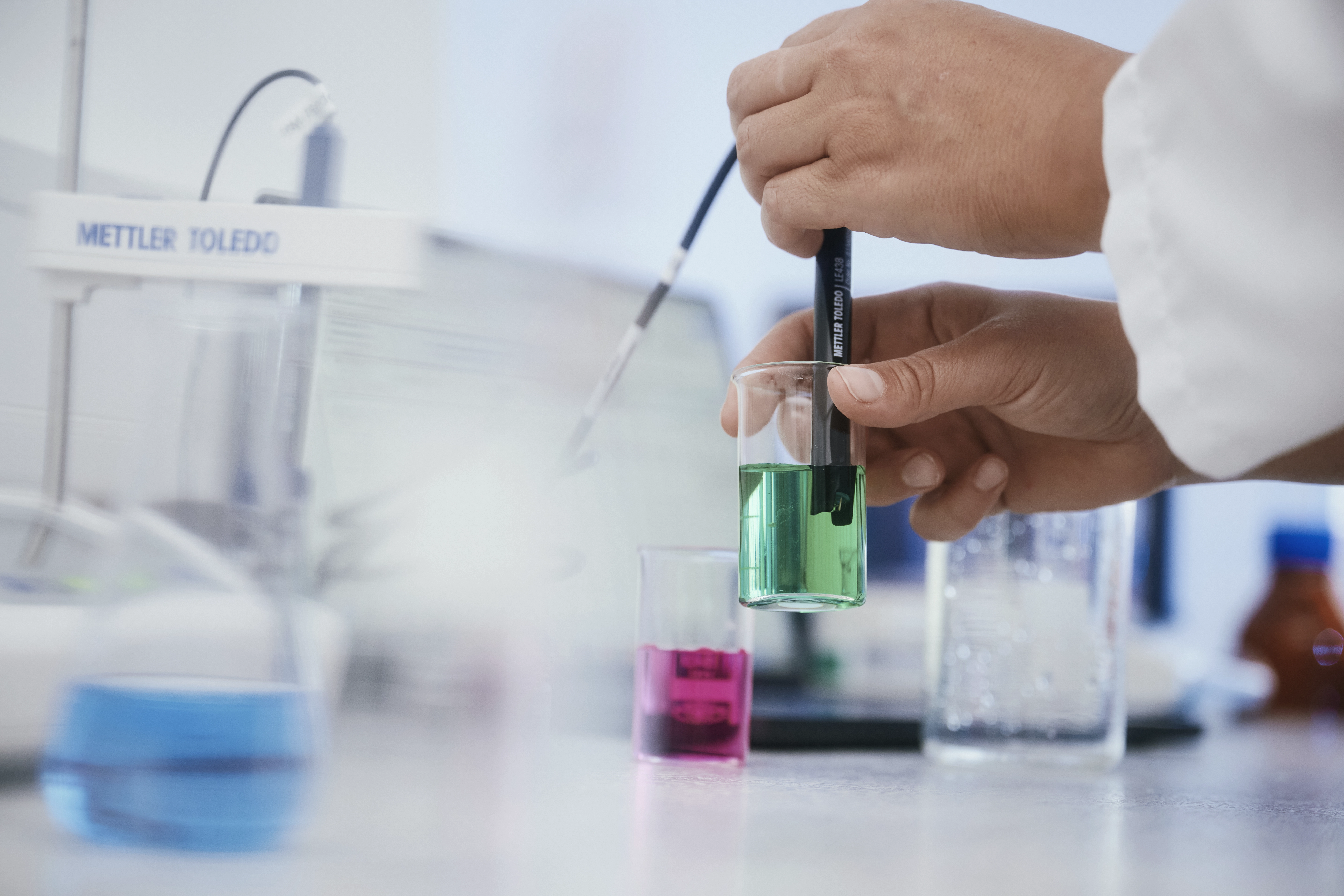 Lab technician measures the pH of a green liquid with a probe during quality control.