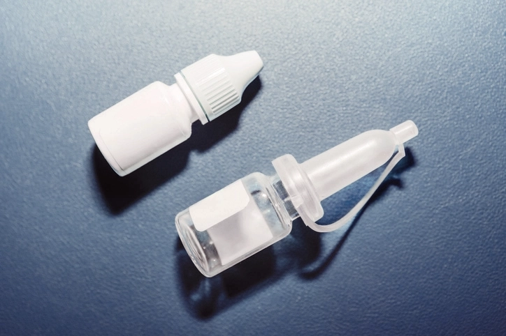 Weißes Tropffläschchen und Applikatorflasche für Medizinprodukte auf blauem Hintergrund.