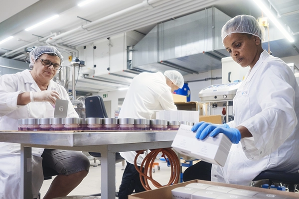Mitarbeiter in der Produktion von ZSB, die gemeinsam an einer Fertigungsstraße für die Abfüllung und Endverpackung von Cremedosen arbeiten