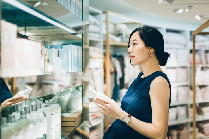 Hübsche Frau steht vor einem Regal mit hochwertig verpackter Kosmetik und Parfum