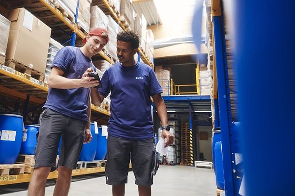 ZSB-Mitarbeiter im Firmenshirt mit einem Kollegen bei der Teamarbeit in der Logistik.